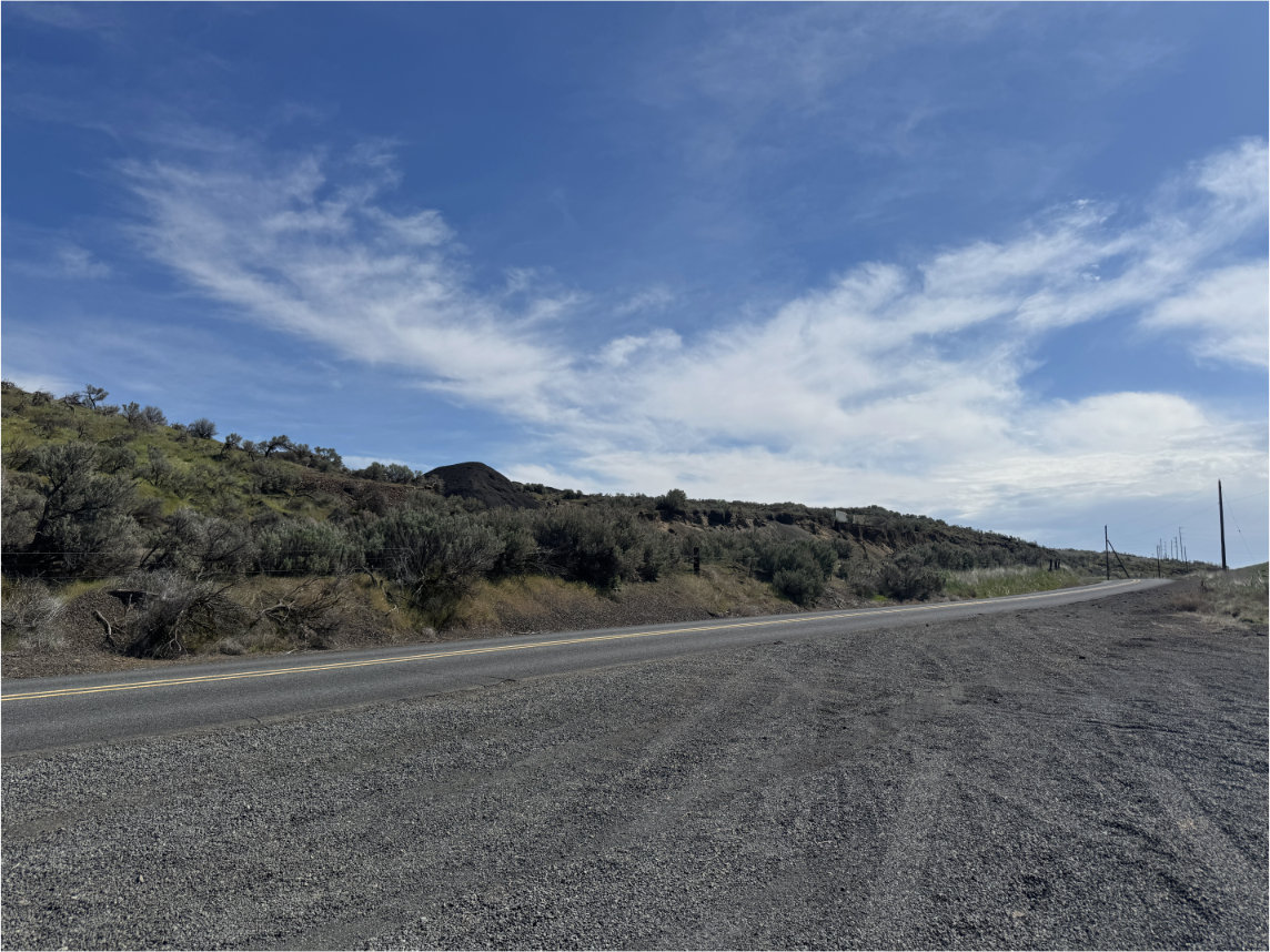 A deserted road looking at a small hill full of desert shrubbery