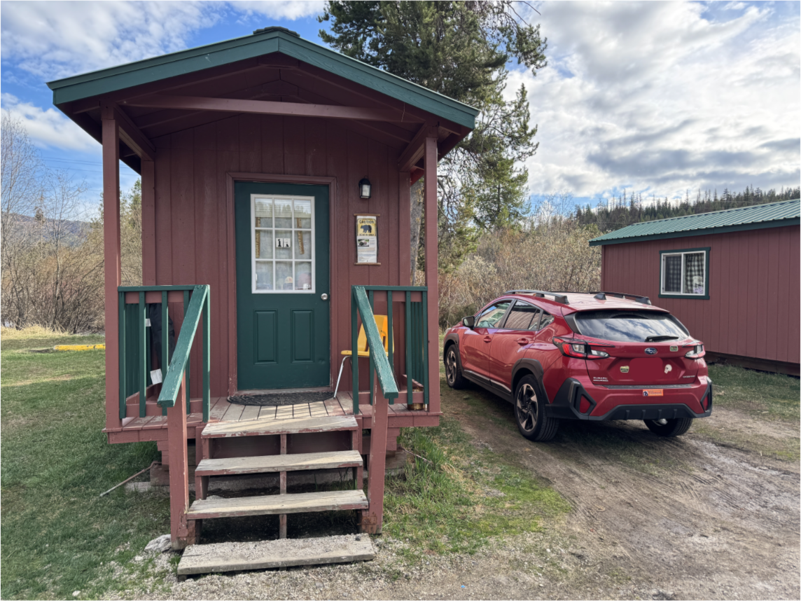 A tiny wooden cabin with a deep red car parked next to it