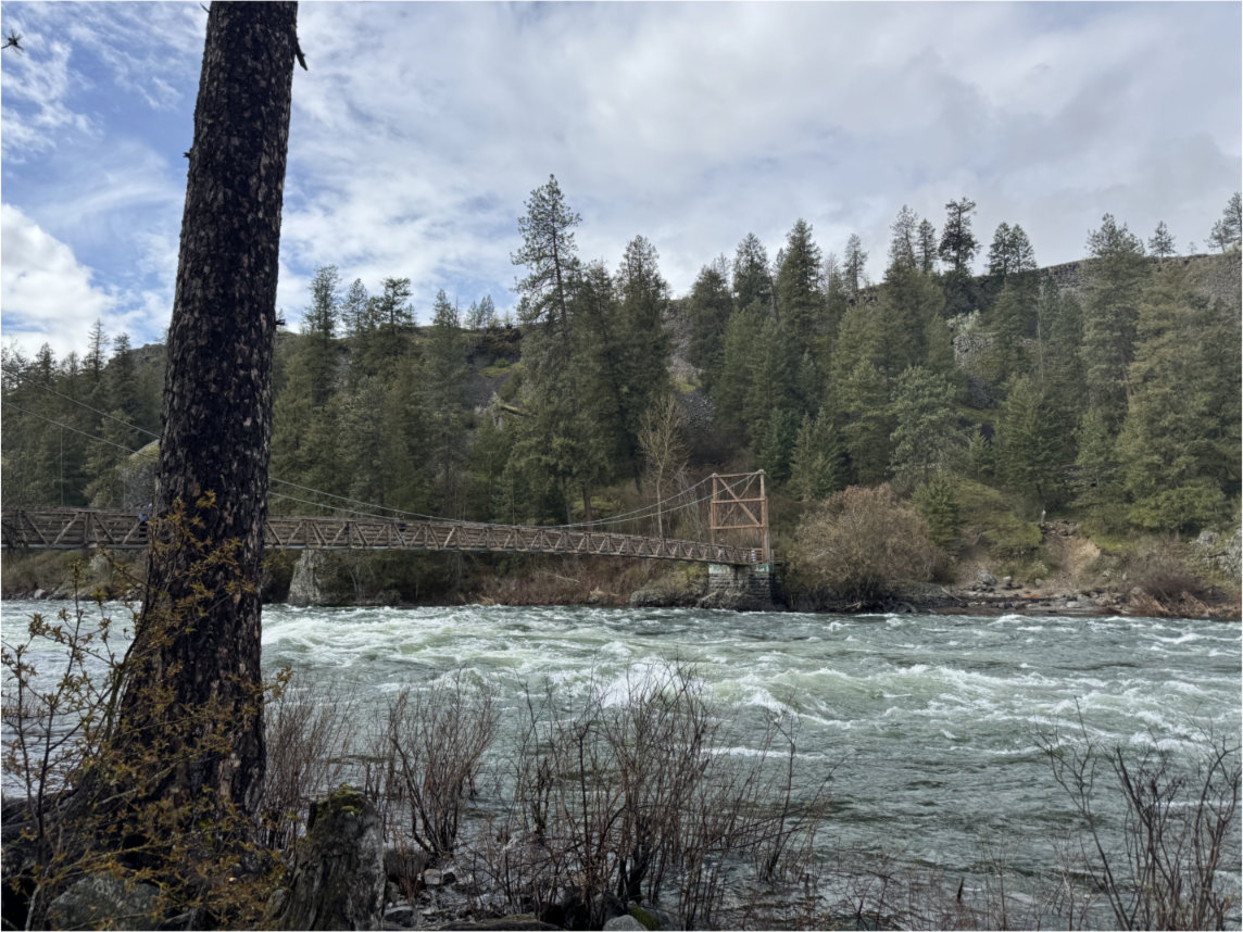 A wooden bridge crosses the turbulent Spokane River