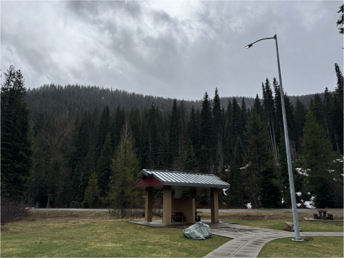 A small rest area with two tables backdropped by a tall mountain as snow falls